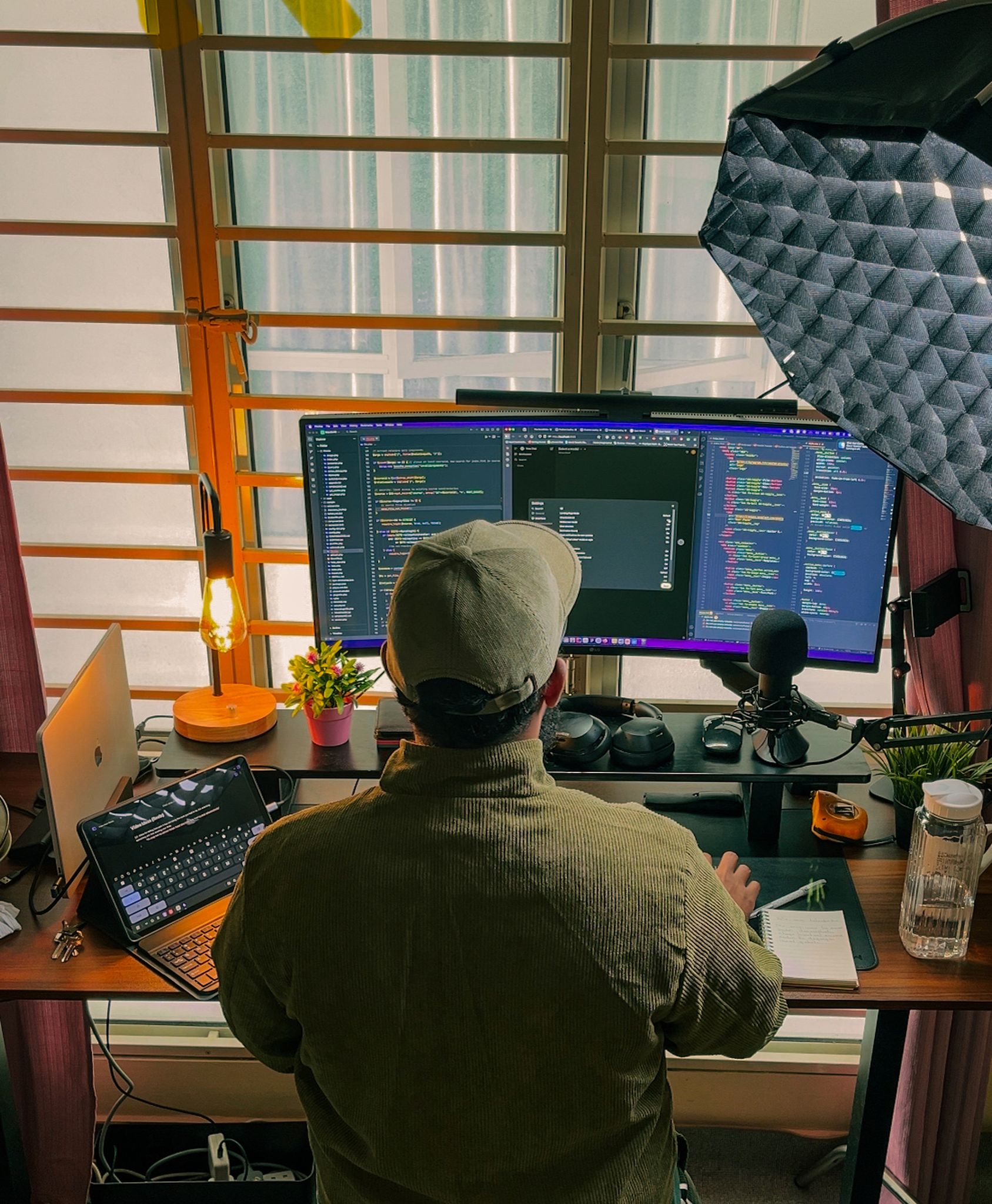 A developer's home office setup with multiple screens, coding in progress, and cozy lighting.